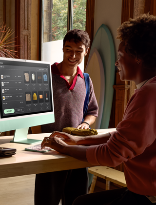 Duas pessoas numa sala bem iluminada a ver produtos no ecrã de vidro de nanotextura do iMac