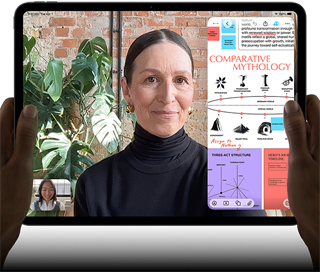 Vista frontal do iPad Pro, preto sideral, colocado na horizontal, ecrã com moldura preta e cantos arredondados, mãos a segurar os lados esquerdo e direito, ecrã apresenta uma conversa no FaceTime com tradução em tempo real e uma app educativa com uma apresentação intitulada