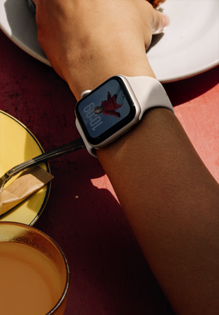 Braço de uma pessoa a tomar o pequeno-almoço, de Apple Watch SE 3 no pulso, com caixa em alumínio luz das estrelas, ecrã Sempre ligado, retrato de uma pessoa no mostrador, Bracelete desportiva luz das estrelas